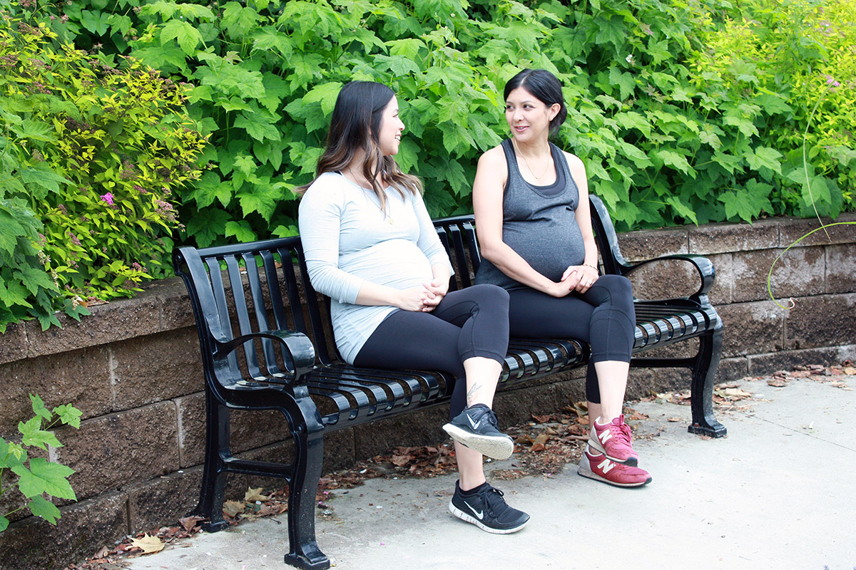 2 pregnant women sitting on a park bench